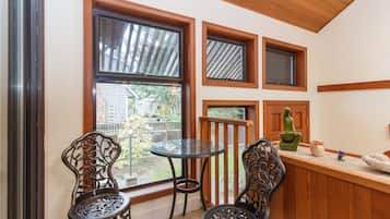 A small room with a glass table and two chairs, a wooden bench, and a window with a view of a backyard.