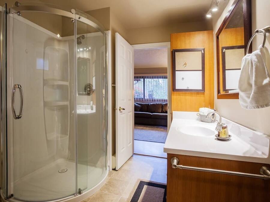 A modern bathroom with a glass-enclosed shower, a wooden vanity with a sink, and a mirror.
