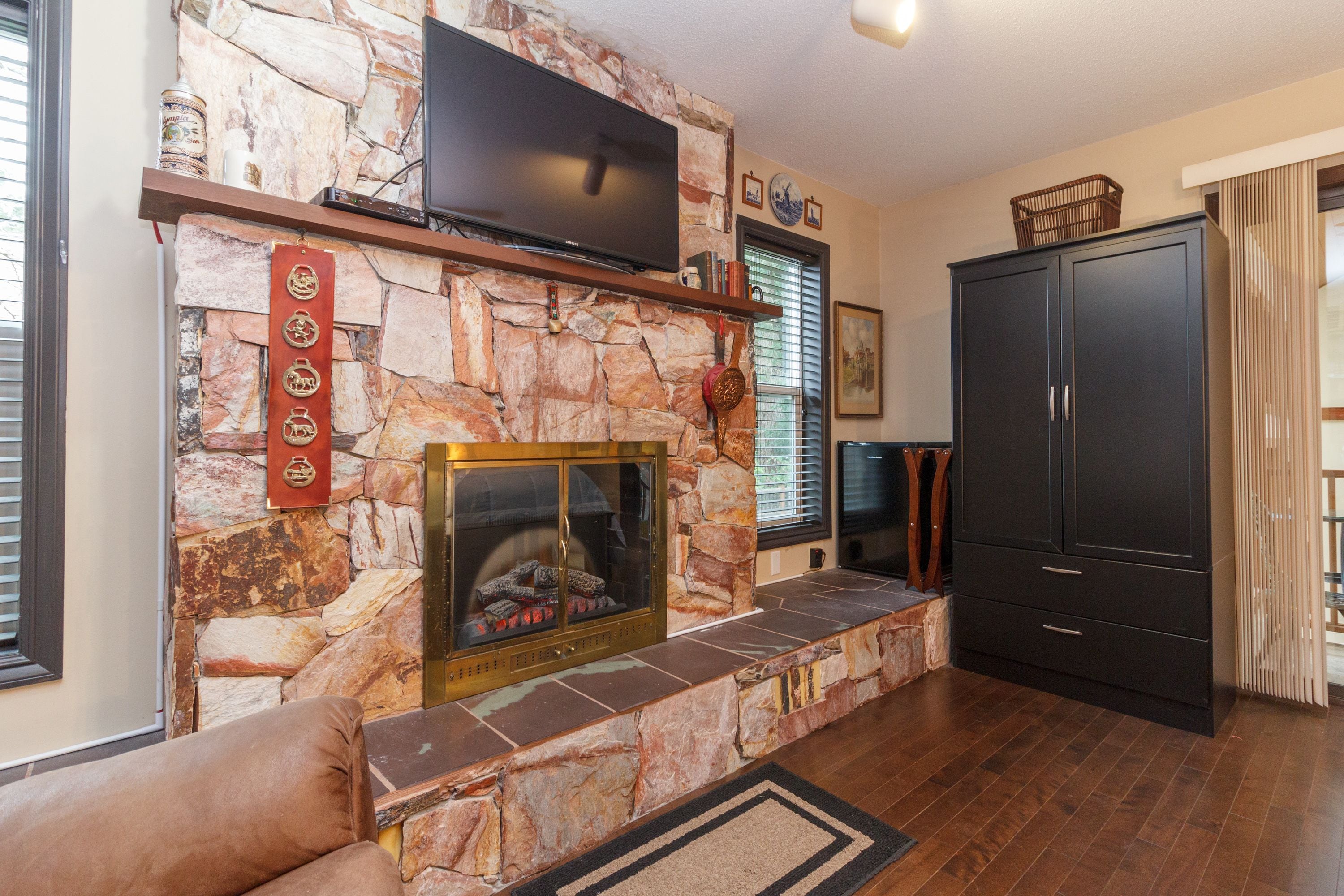 A stone fireplace with a television above it, a wooden cabinet, and a cushioned seating area.
