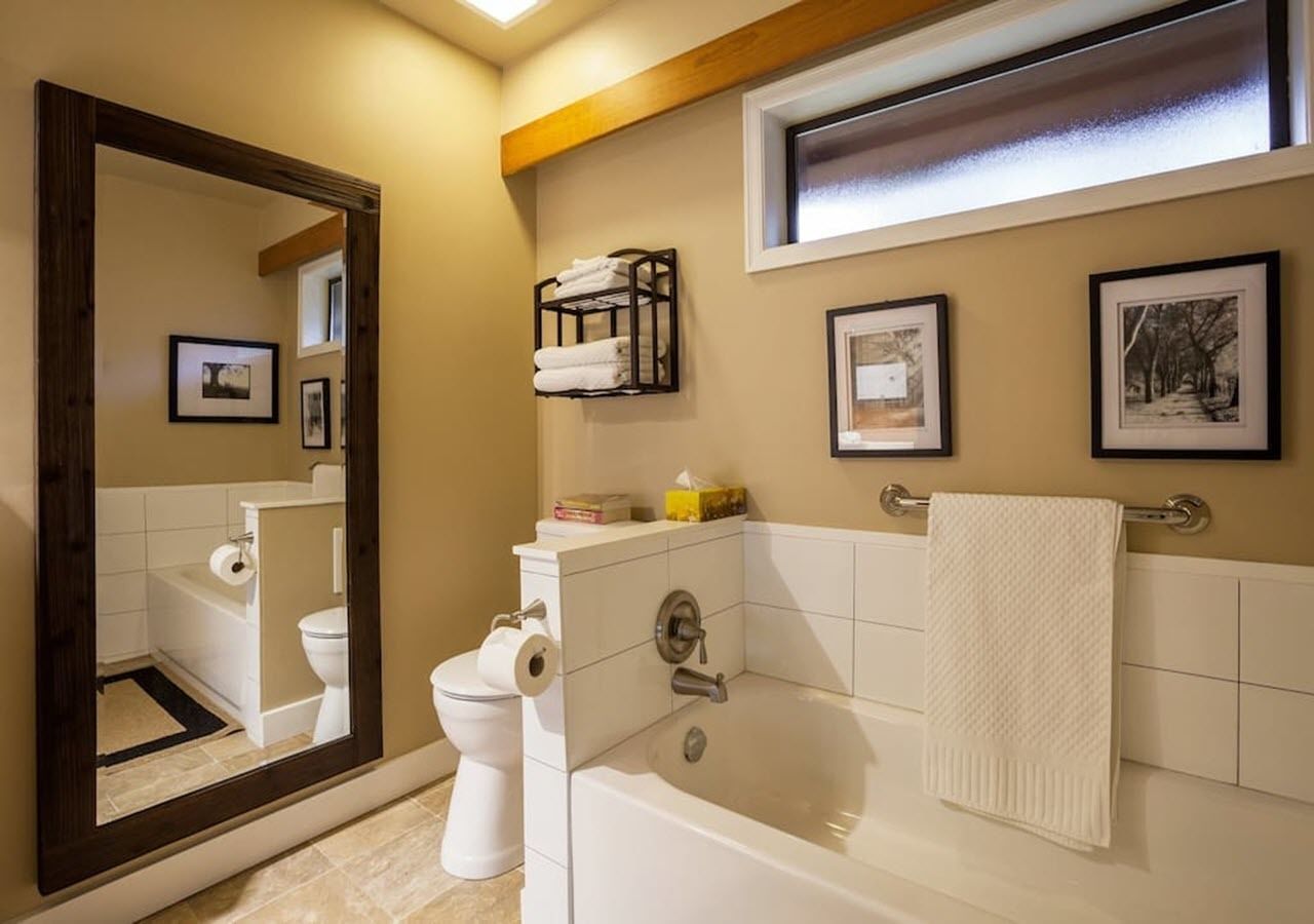 Un baño con bañera, inodoro y un espejo grande.