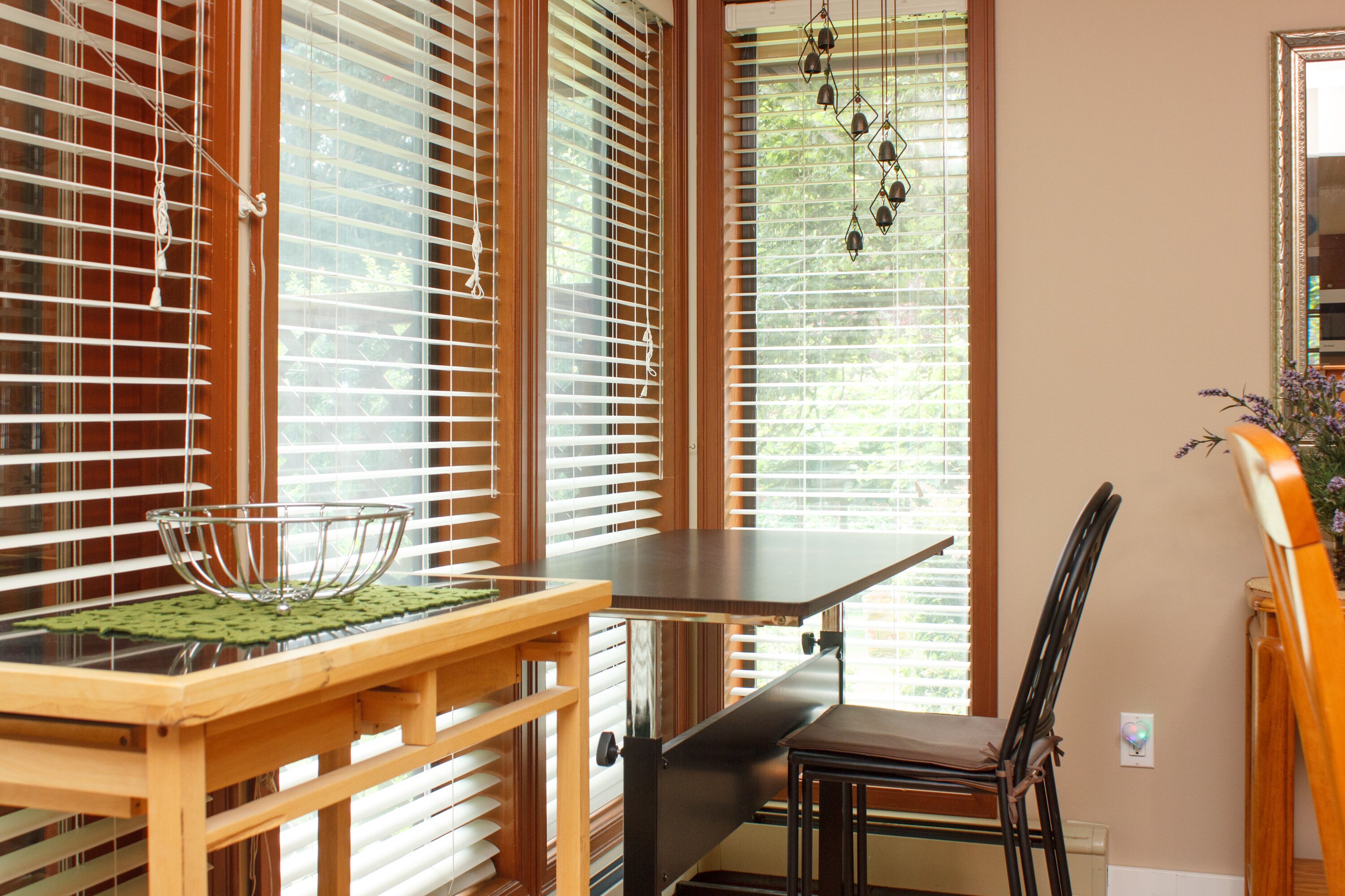 A dining area with a wooden table and chairs, a glass bowl on the table, and a view through the window with blinds.