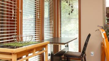 A dining area with a wooden table and chairs, a glass bowl on the table, and a view through the window with blinds.