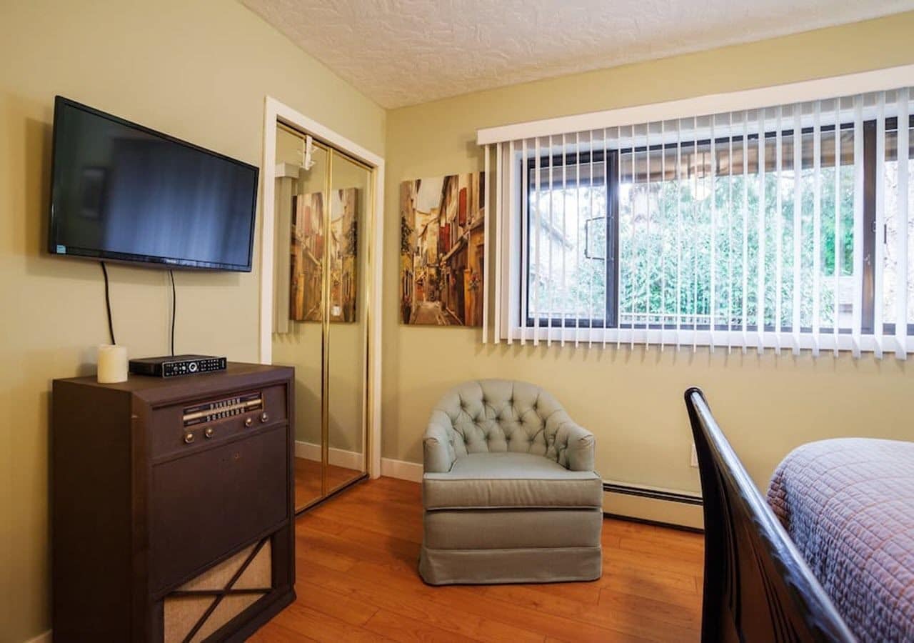 A room with a TV, a vintage radio, a tufted armchair, and a bed.