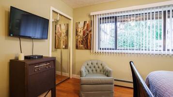 A room with a TV, a vintage radio, a tufted armchair, and a bed.