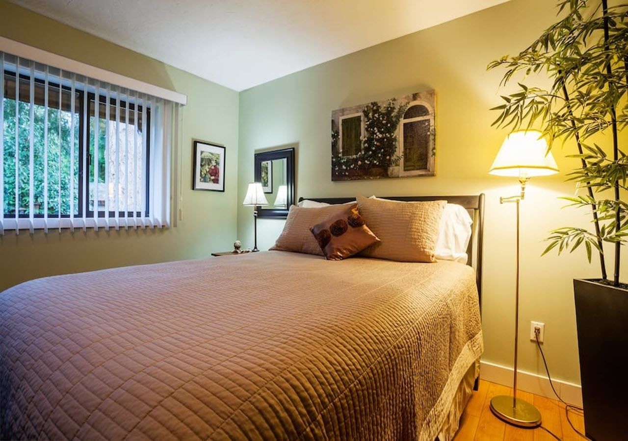 Un dormitorio con una cama grande, una mesita de noche, una lámpara y una ventana con persianas.