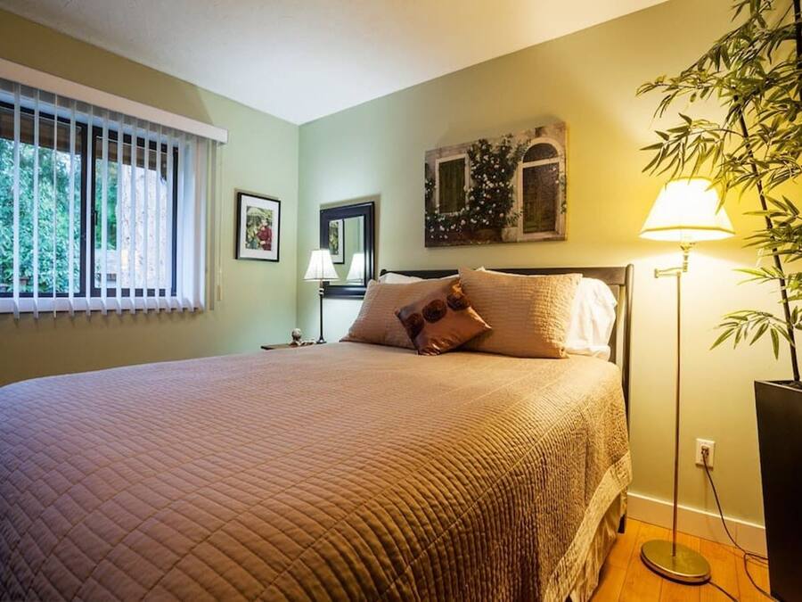 Un dormitorio con una cama grande, una mesita de noche, una lámpara y una ventana con persianas.