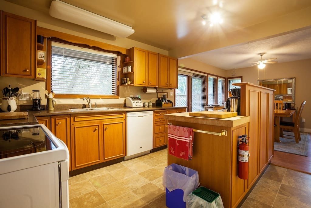 A kitchen with wooden cabinets, a dishwasher, a stove, and a window with blinds.