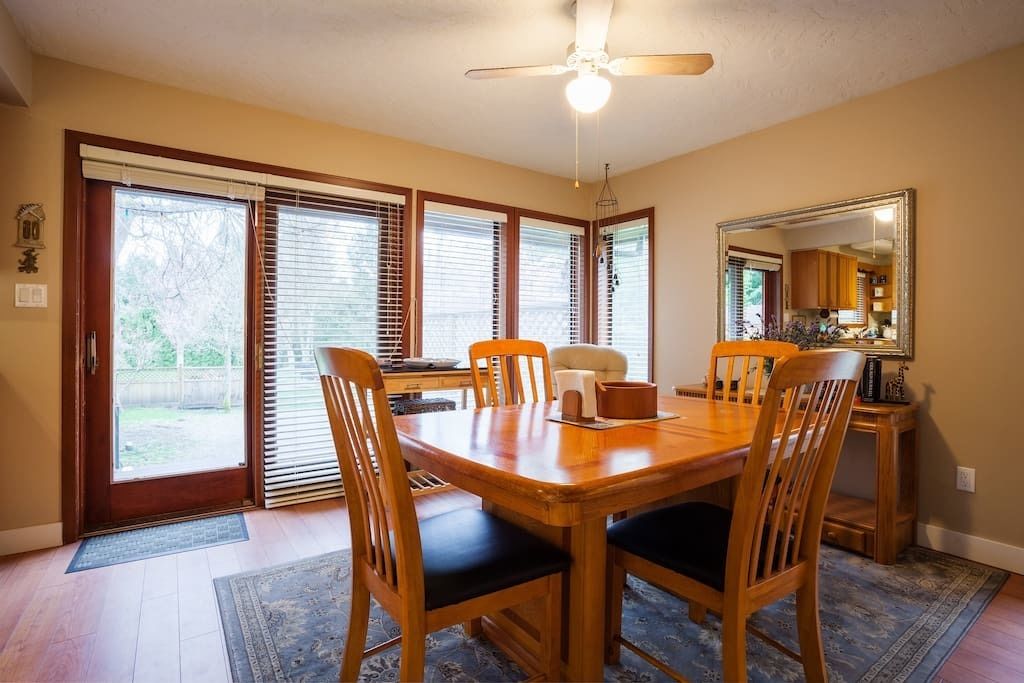 A dining area with a wooden table and chairs, a ceiling fan, and a view of the backyard through large sliding glass doors.