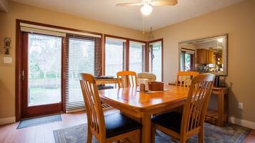 A dining area with a wooden table and chairs, a ceiling fan, and a view of the backyard through large sliding glass doors.