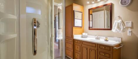 A modern bathroom with a glass shower enclosure, wooden vanity, and a large mirror.