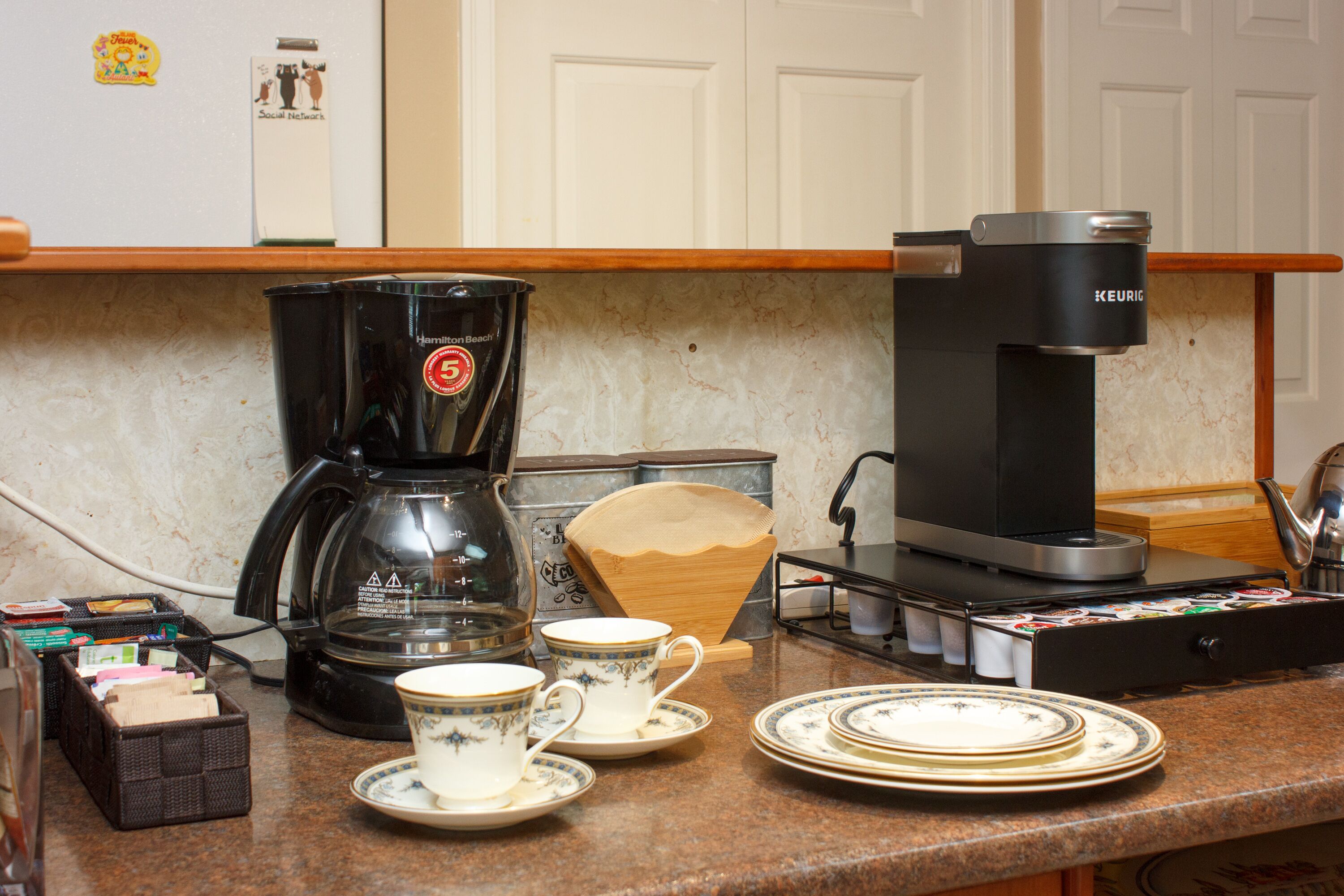 A kitchen counter with a coffee maker, cups, and plates.