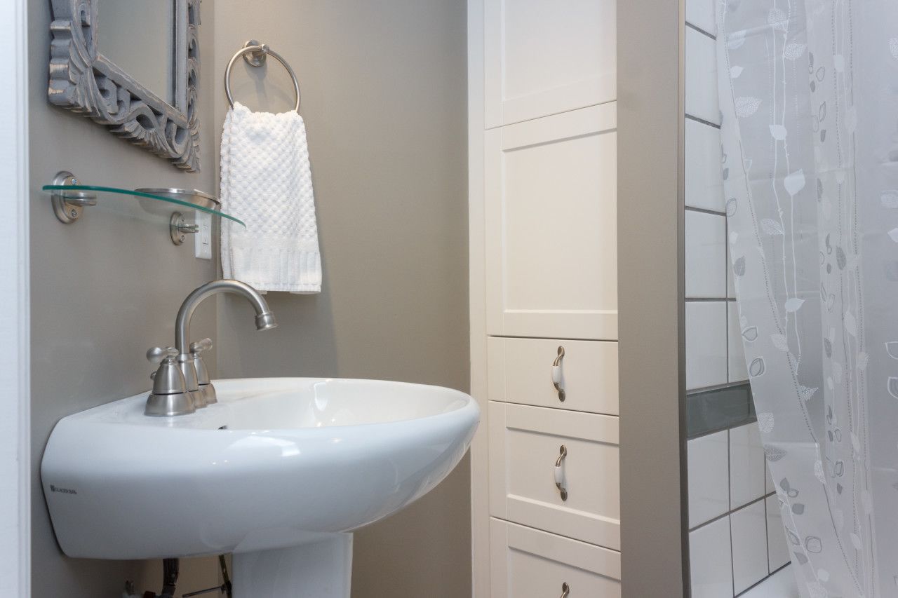 A bathroom with a white sink, a glass shelf, a towel ring, and a white cabinet with drawers.