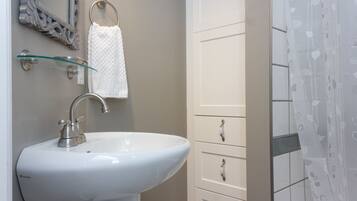 A bathroom with a white sink, a glass shelf, a towel ring, and a white cabinet with drawers.