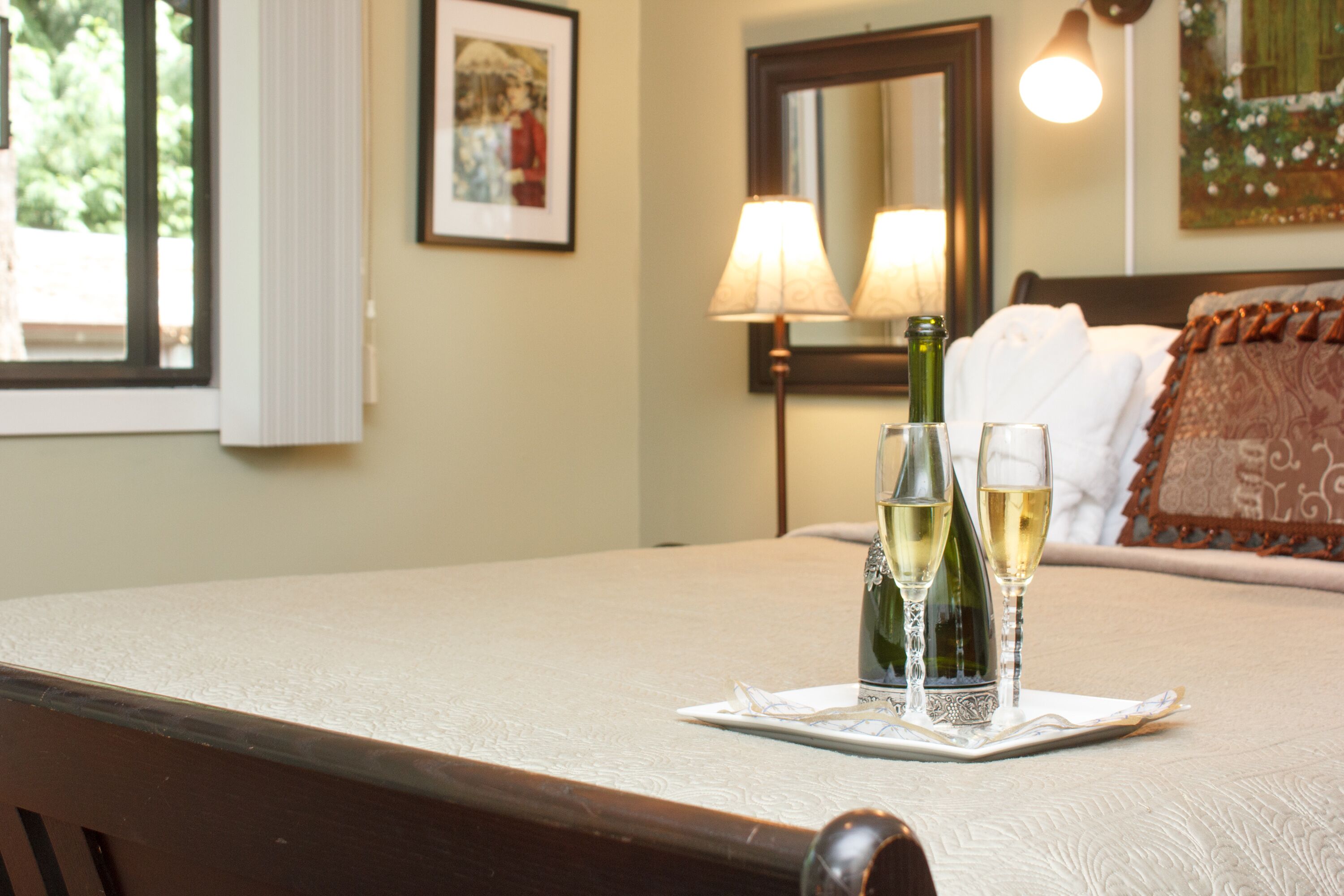 Un lit bien fait, avec un oreiller, une table de chevet sur laquelle se trouve une lampe, et deux bouteilles de champagne sur un plateau.