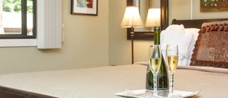 A neatly made bed with a pillow, a bedside table with a lamp, and two bottles of champagne on a tray.