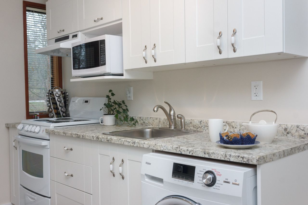 A compact kitchen with white cabinets, a built-in microwave, a stainless steel sink, a stove, and a dishwasher.
