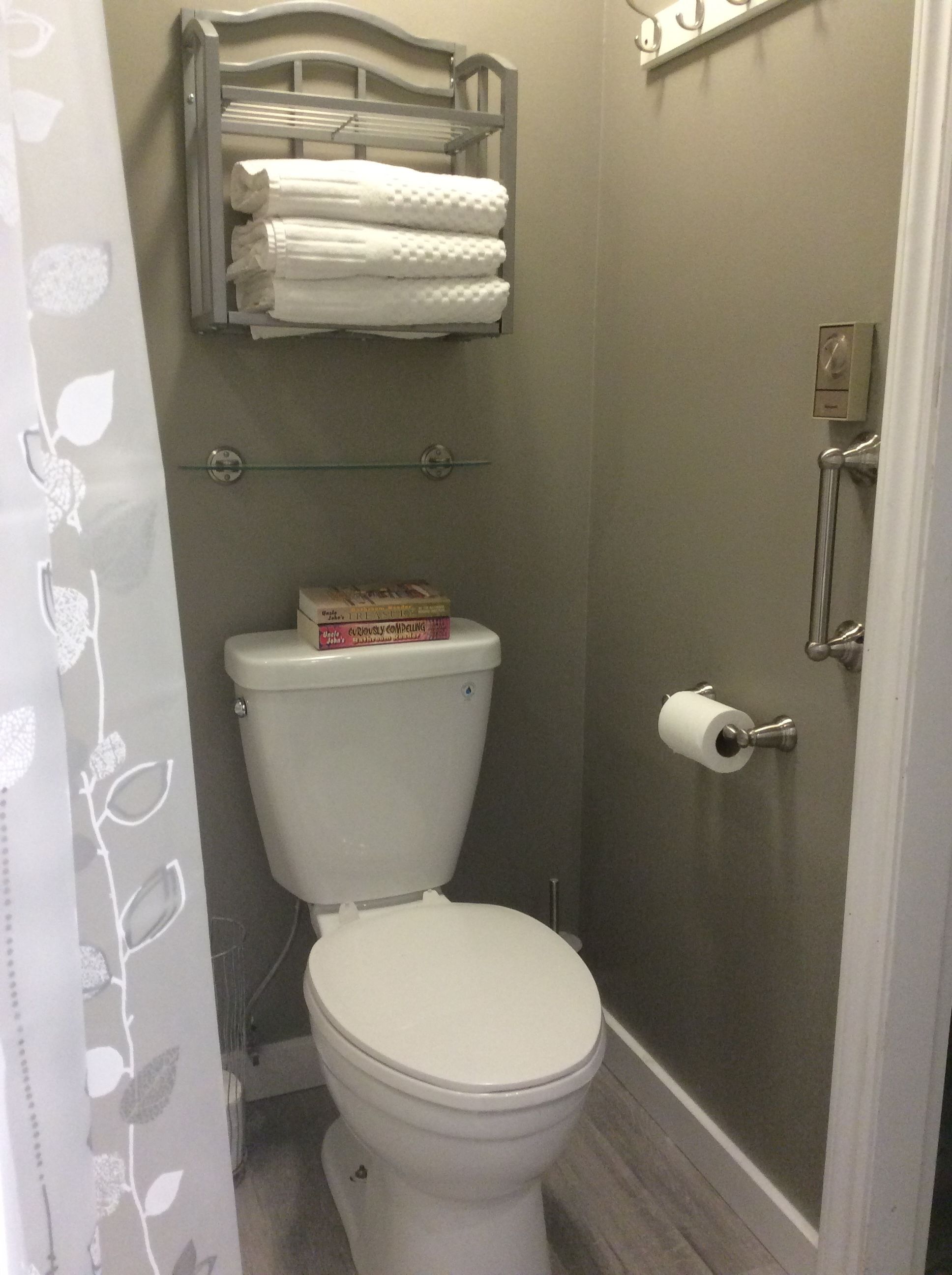 Een badkamer met een toilet, een plank met handdoeken en een toiletpapierhouder.