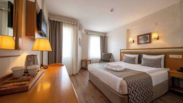 Una habitación de hotel con cama, mesita de noche, lámpara, televisión y una pequeña mesa con tazas y bandeja.