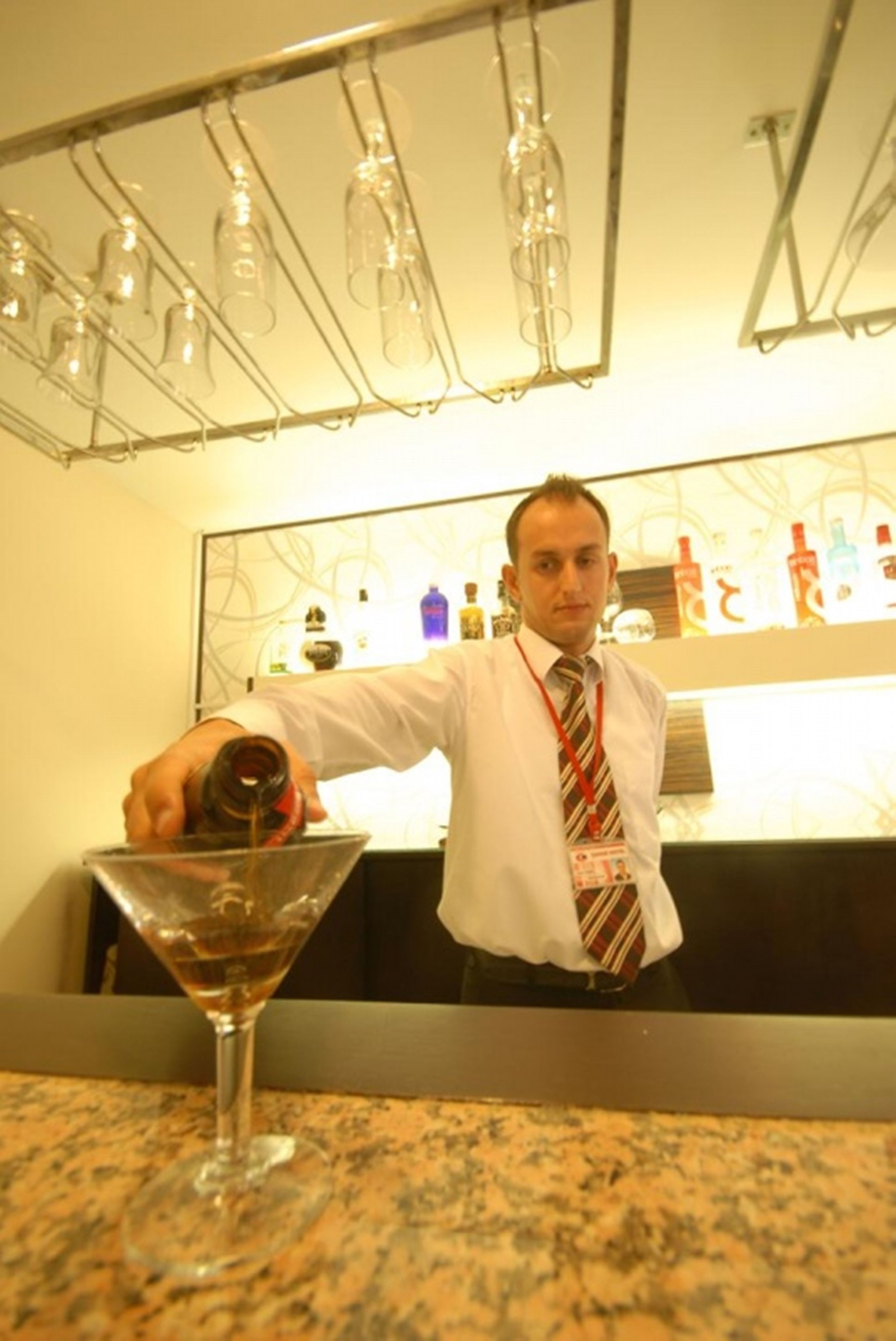 Uma área de bar com um bartender servindo uma bebida num copo de martini.