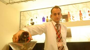 Uma área de bar com um bartender servindo uma bebida num copo de martini.