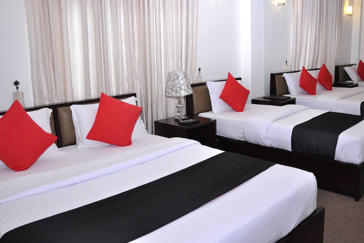 Une chambre d’hôtel avec deux lits, chacun doté de draps blancs et d’oreillers rouges, une table de chevet avec une lampe et une grande fenêtre avec des rideaux.