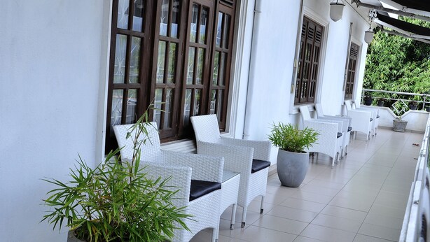 A covered outdoor seating area with white wicker furniture and potted plants. - Laa Adams (Hatton)