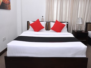 A hotel room with a bed, two red pillows, a black bed runner, a nightstand with a lamp, and a curtain. - Laa Adams (Hatton)