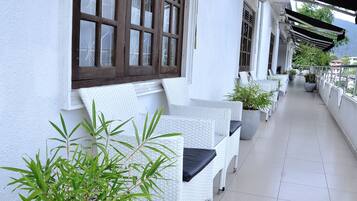Un espacio al aire libre con techo, mobiliario de mimbre blanco y plantas en macetas.