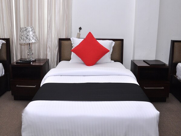 A hotel room with a neatly made bed, a red pillow, a lamp, and a nightstand with a remote control. - Laa Adams (Hatton)