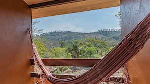 A hammock on a balcony with a view of a green landscape and hills. - Wood House (Petrópolis)