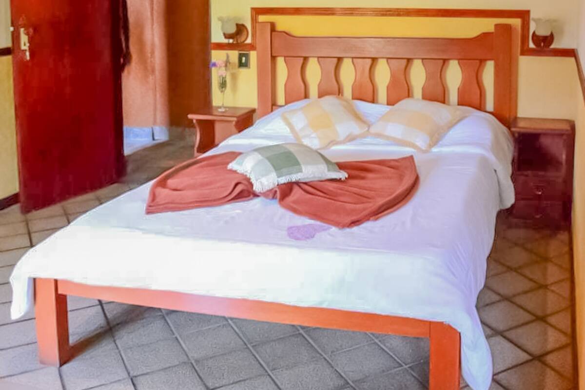 Une chambre d’hôtel avec un lit en bois, une porte rouge, un sol carrelé et un plafond en bois.