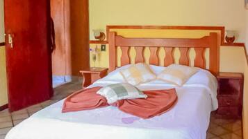 Een hotelkamer met een houten bed, een rode deur, een betegelde vloer en een houten plafond.