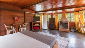 A wooden cabin room with a bed, a television, a fireplace, and a dining area. - Wood House (Petrópolis)
