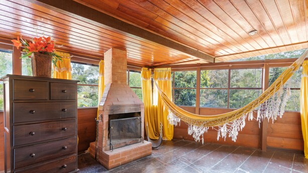 A wooden interior with a fireplace, a wooden dresser, and a hammock. - Wood House (Petrópolis)