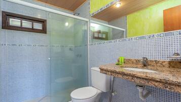 Casa de banho com chuveiro em cabine de vidro, sanita branca e bancada de granito com lavatório.