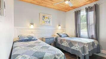 A bedroom with two beds, wooden ceiling, ceiling fan, window with curtains, and wall-mounted light fixtures.