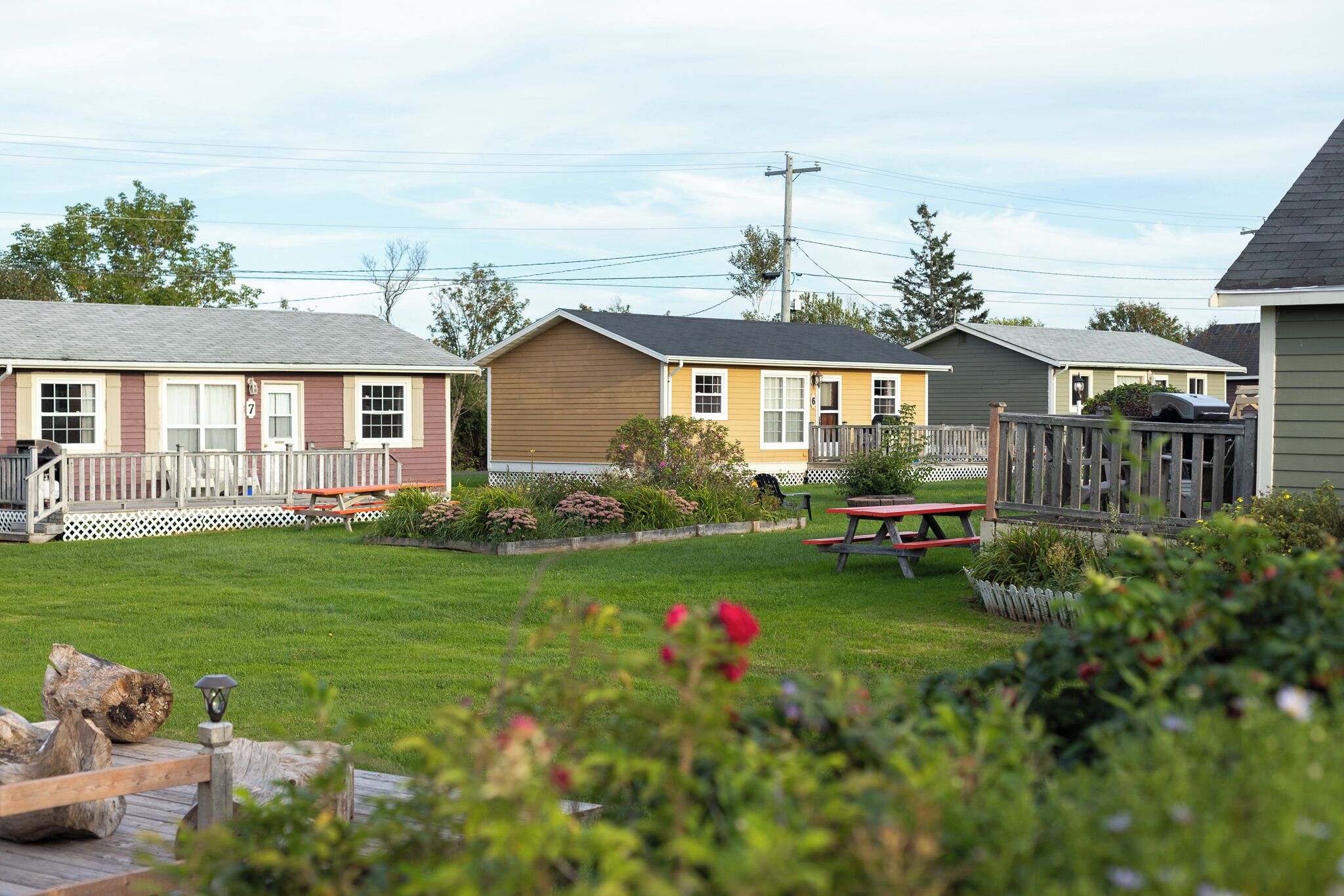 A row of mobile homes with a grassy yard, picnic tables, and a wooden deck.