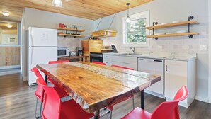 A modern kitchen with a wooden table, red chairs, white cabinets, and a window with a view of trees. - Avonlea Cottages (Cavendish)