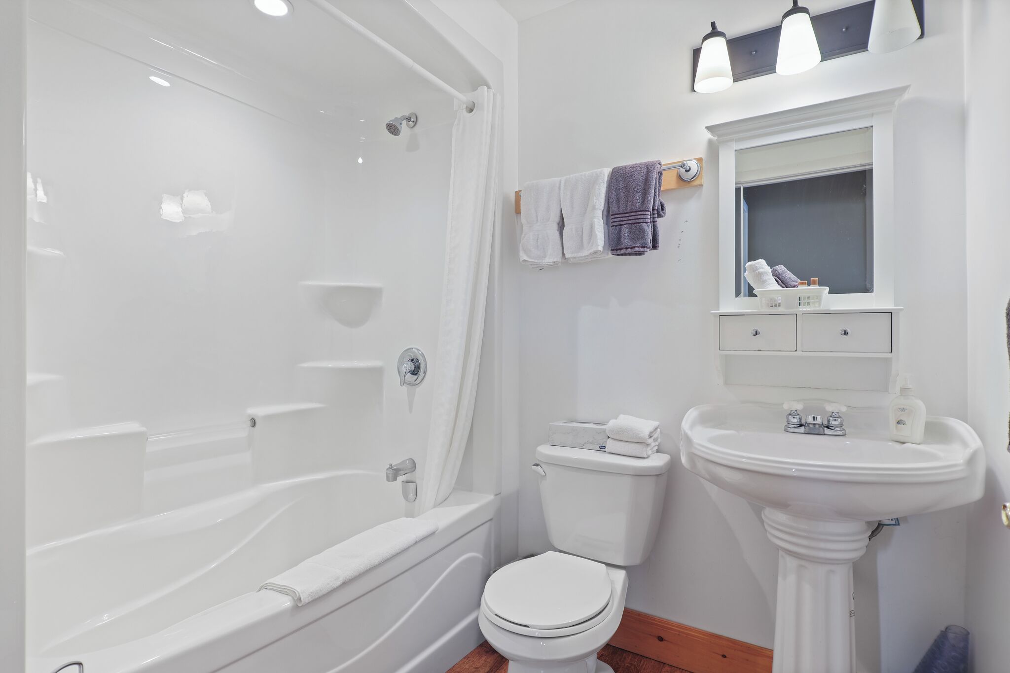 A modern bathroom with a bathtub, toilet, and pedestal sink.
