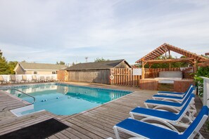 Una terraza de madera con piscina, sillas de descanso y una pérgola de madera.
