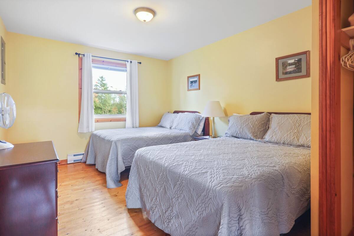 Ein Zimmer mit zwei Betten, einem Holzschrank, einem Fenster mit Vorhängen und einem Deckenventilator.