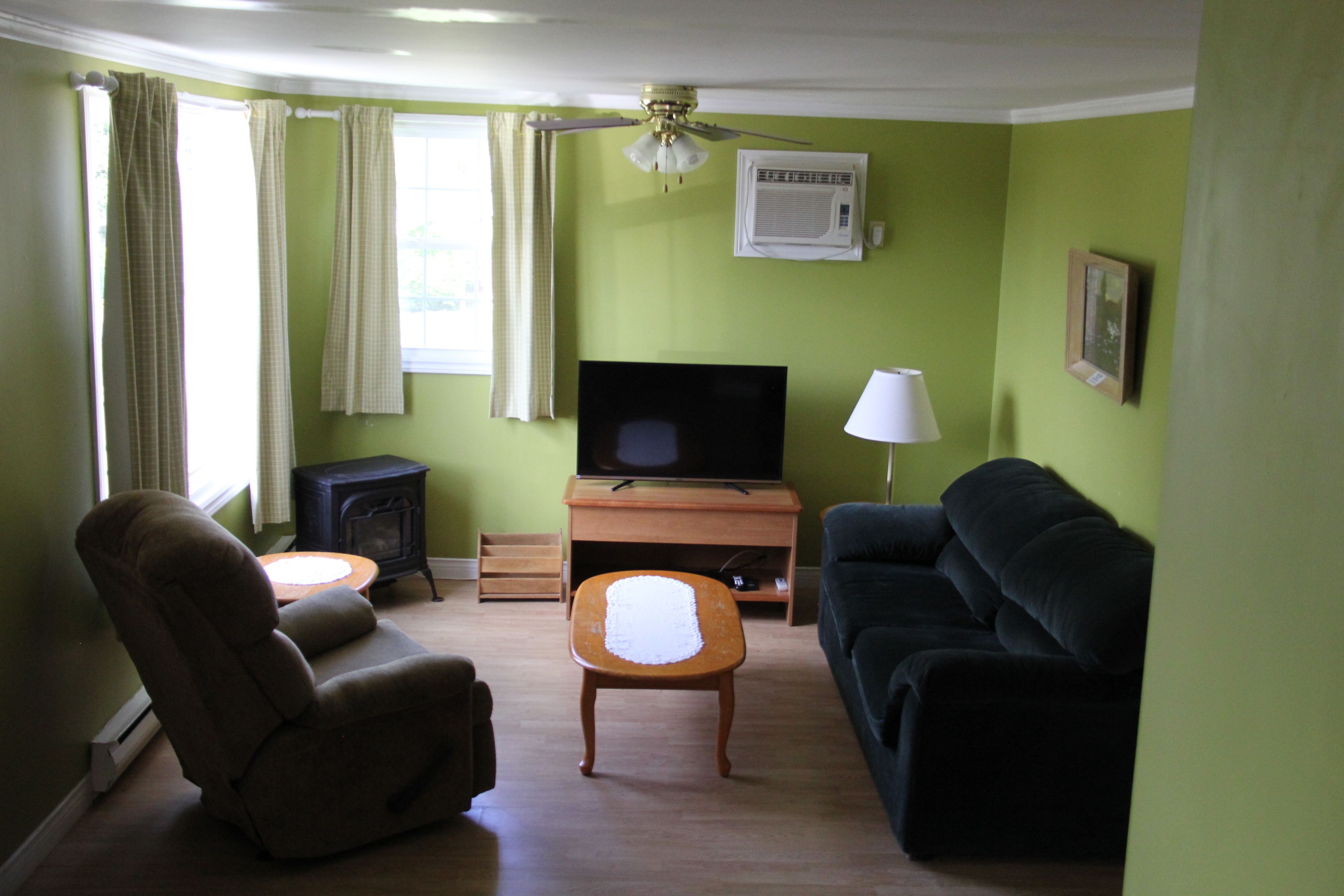 A living room with a television, a sofa, a chair, a small table, and a heater.