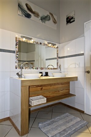 A bathroom with a wooden vanity, two sinks, a mirror with lights, and decorative tiles.