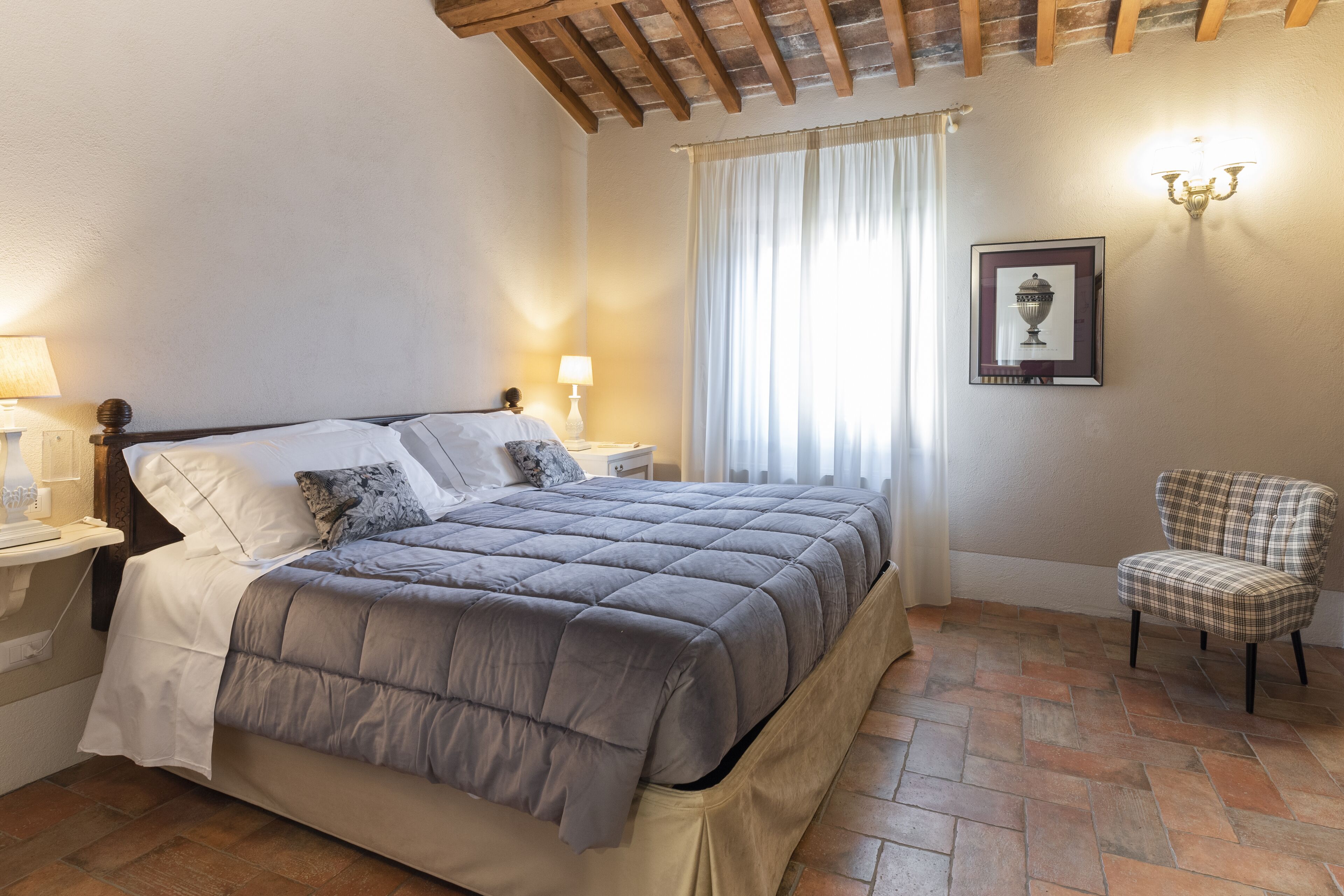 A bedroom with a bed, nightstands, a chair, and a wall-mounted lamp.