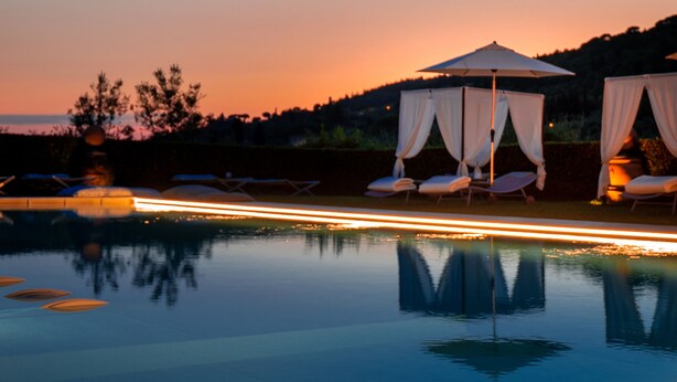 Un espace piscine paisible au crépuscule, avec deux chaises longues abritées par un auvent et un reflet limpide sur l’eau.