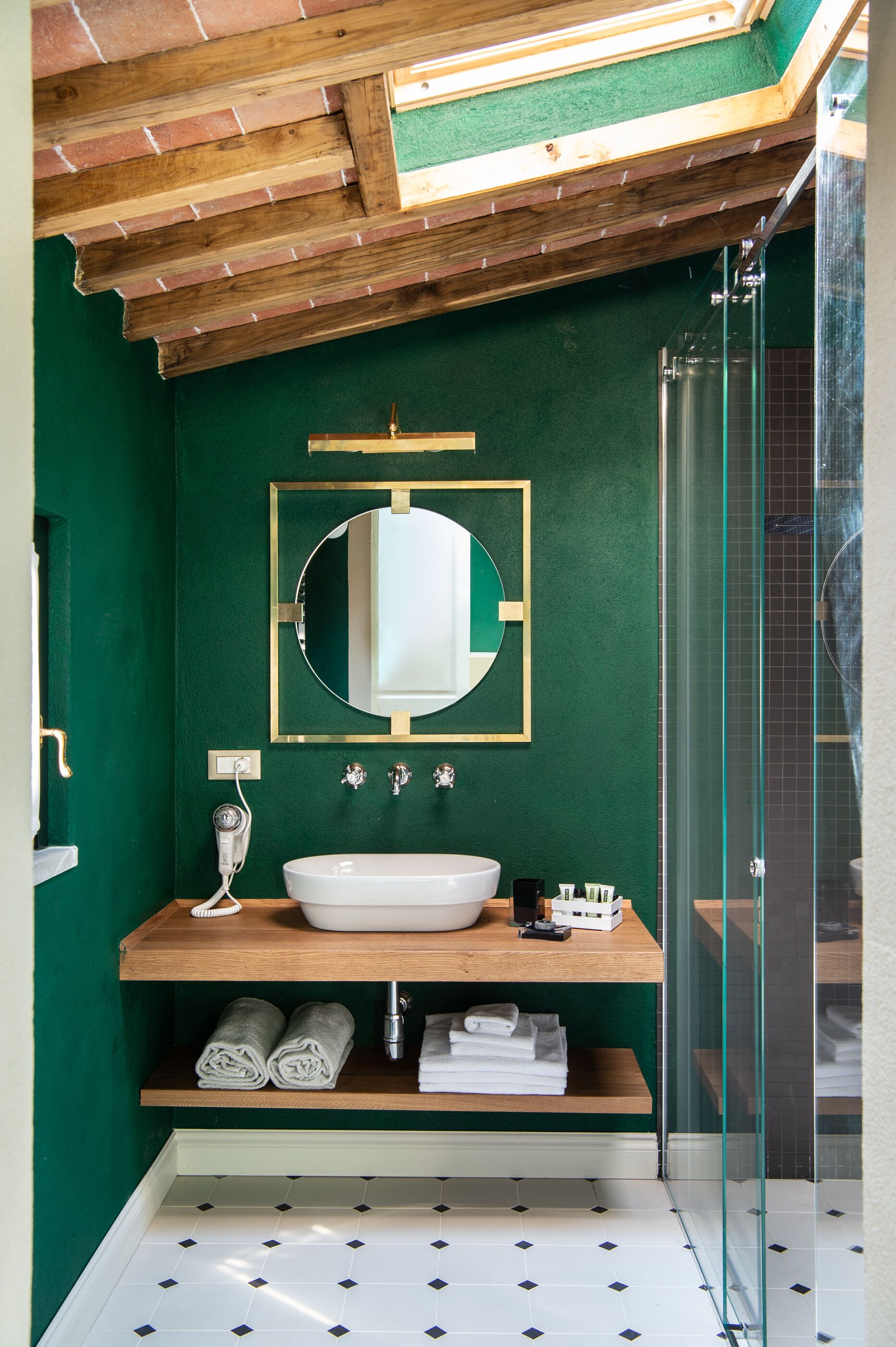 A bathroom with a green wall, a wooden vanity, a white sink, a mirror, and a glass shower enclosure.