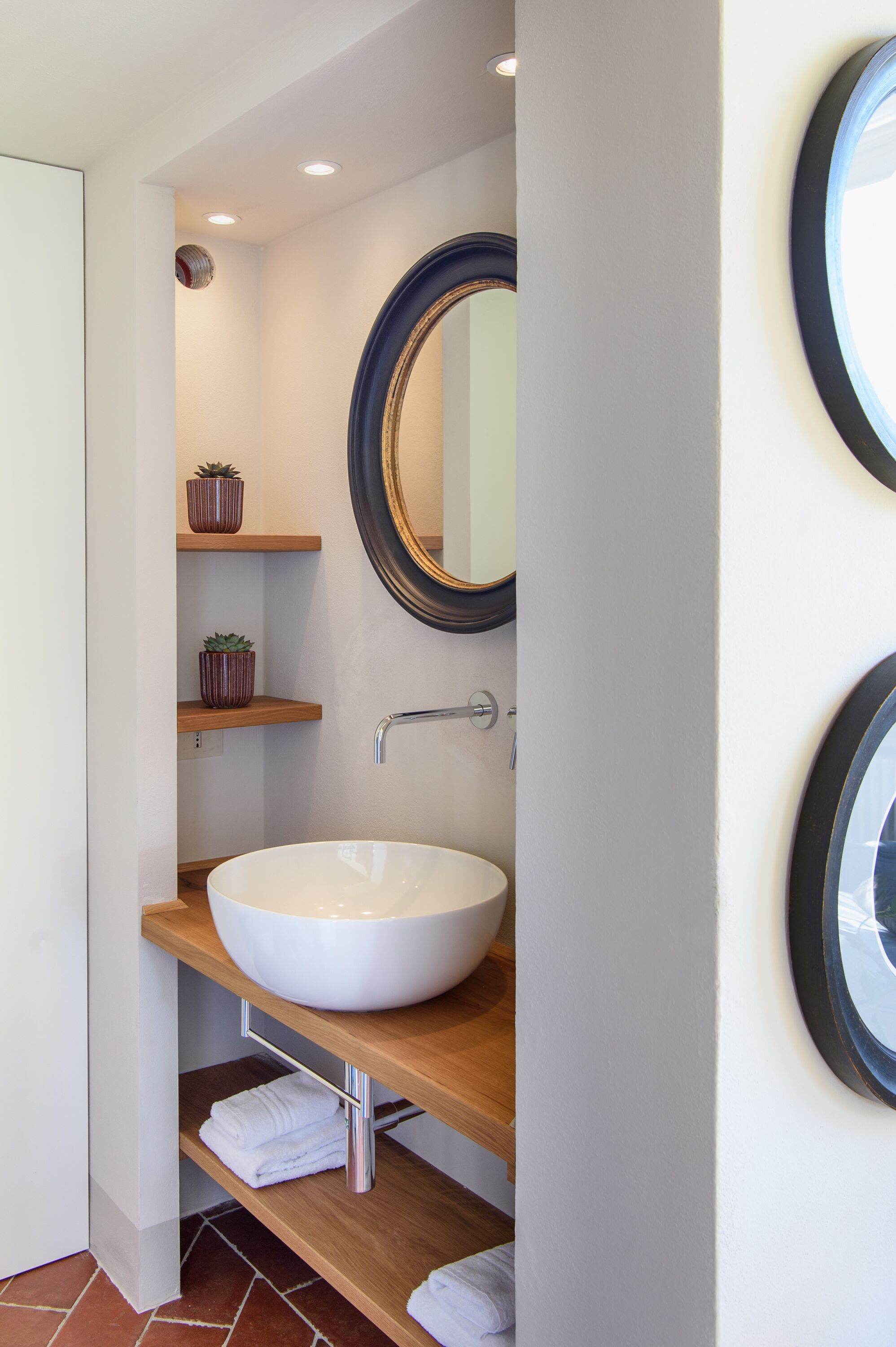 A modern bathroom with a large white sink, wooden shelves, and a mirror.