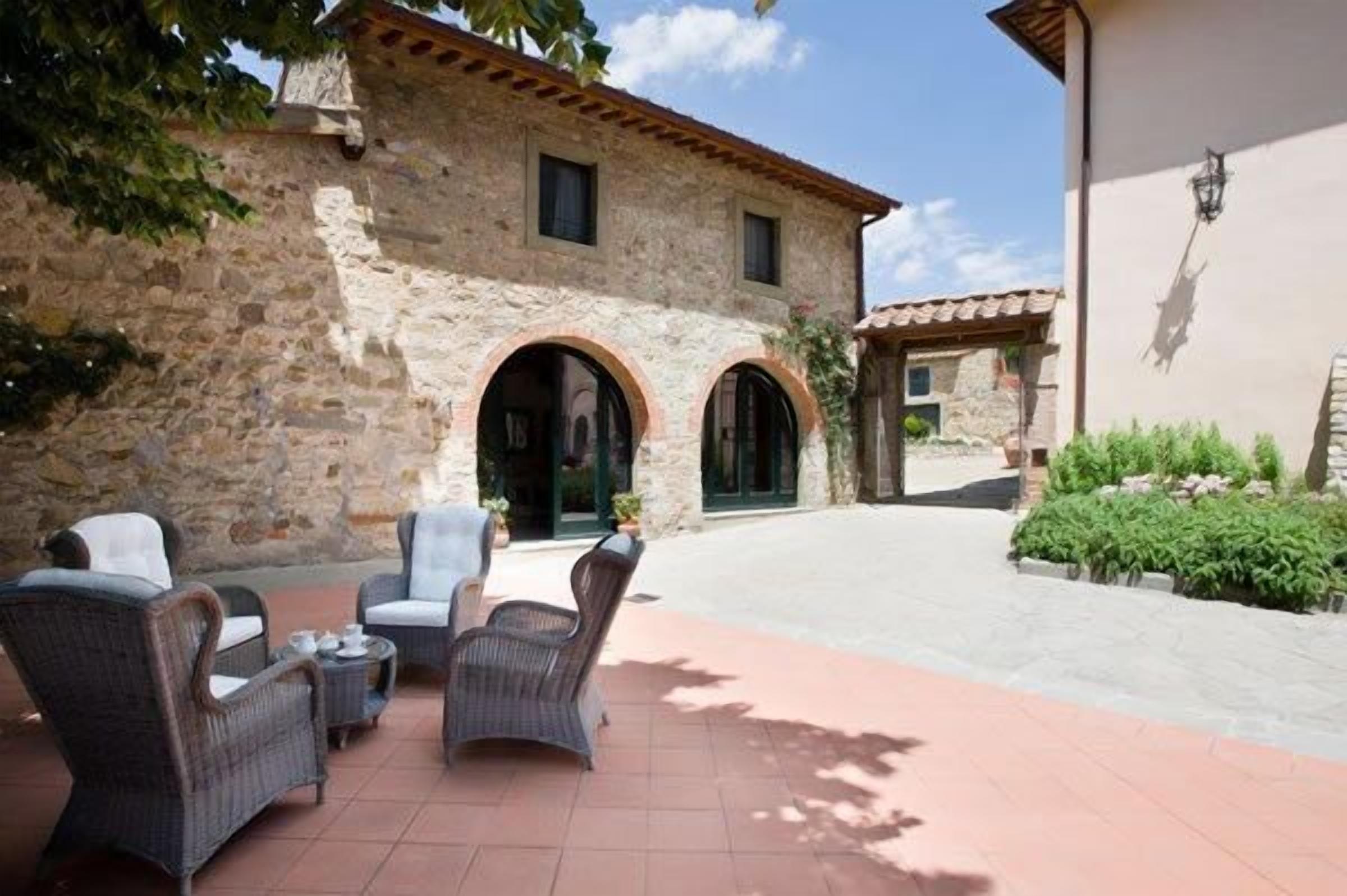 Un edificio de piedra con arcos, mobiliario de mimbre exterior y un patio empedrado.
