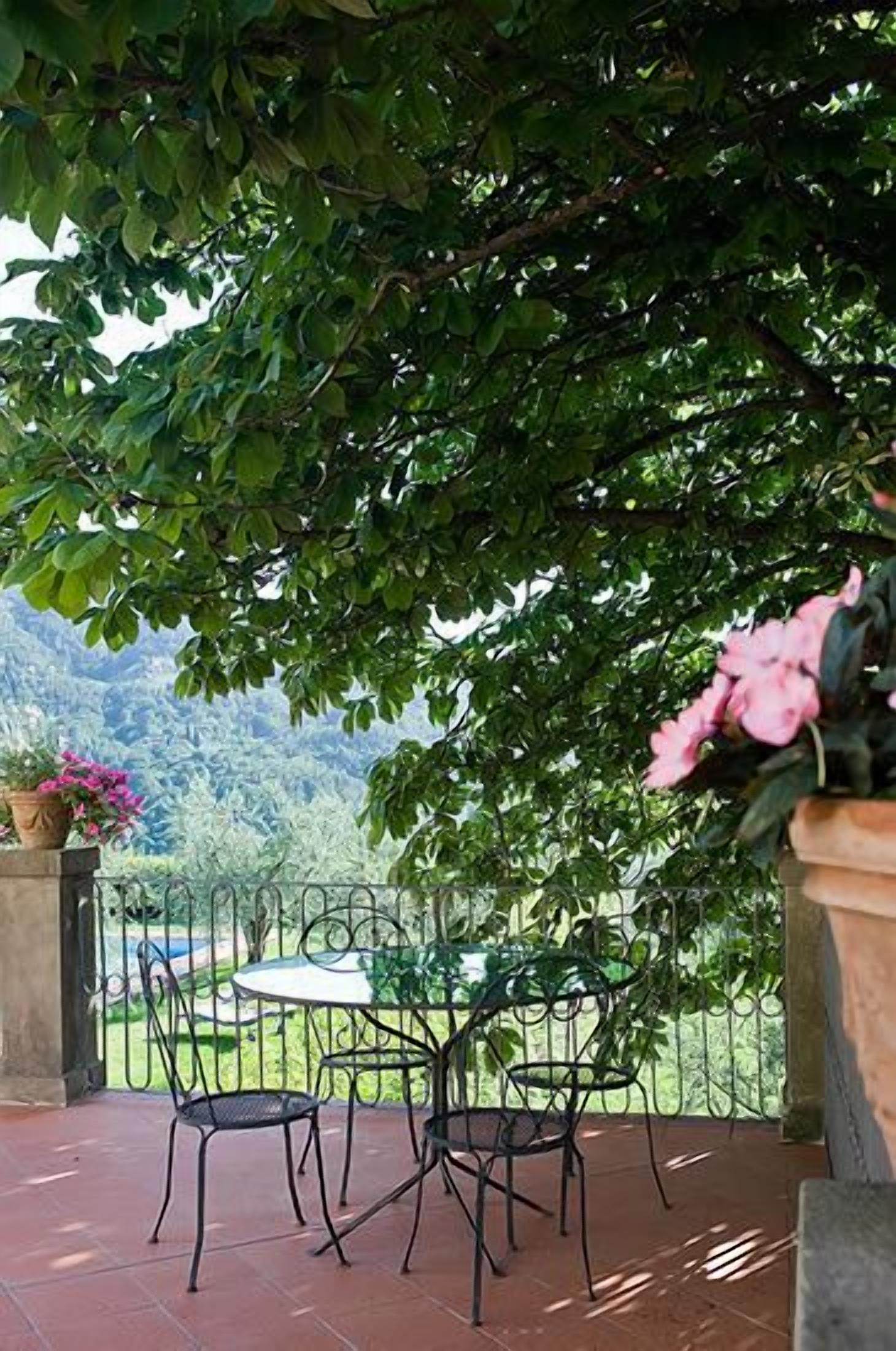 A patio with two metal chairs and a table, surrounded by lush greenery and a mountainous backdrop.