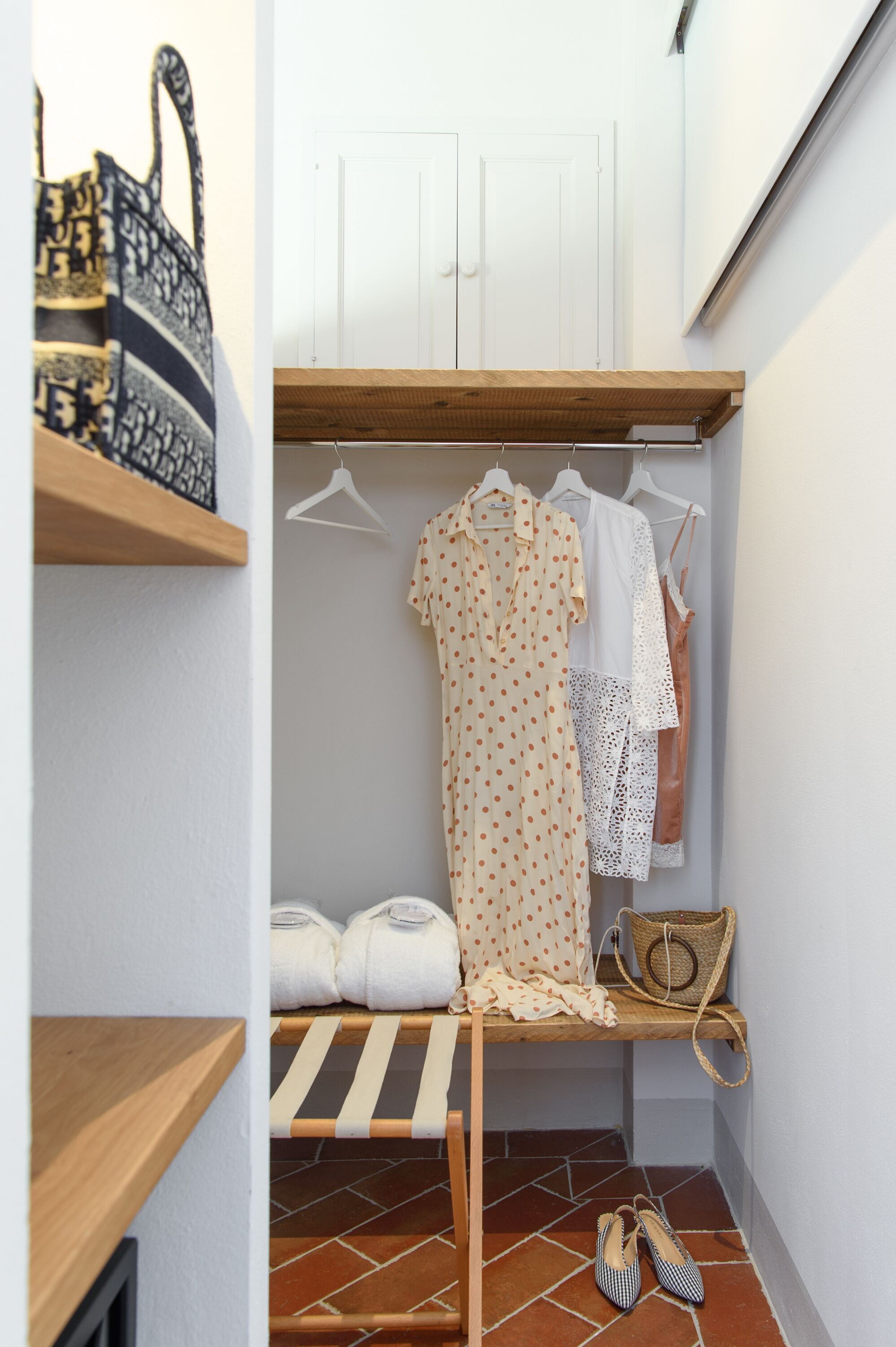 Un petit placard bien rangé, avec des vêtements suspendus, une étagère en bois et un étendoir.
